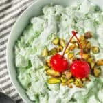 green fluff dessert in a white bowl topped with cherries and chopped nuts