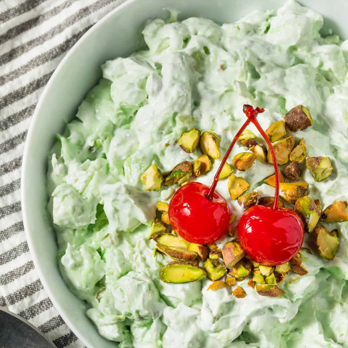 green fluff dessert in a white bowl topped with cherries and chopped nuts