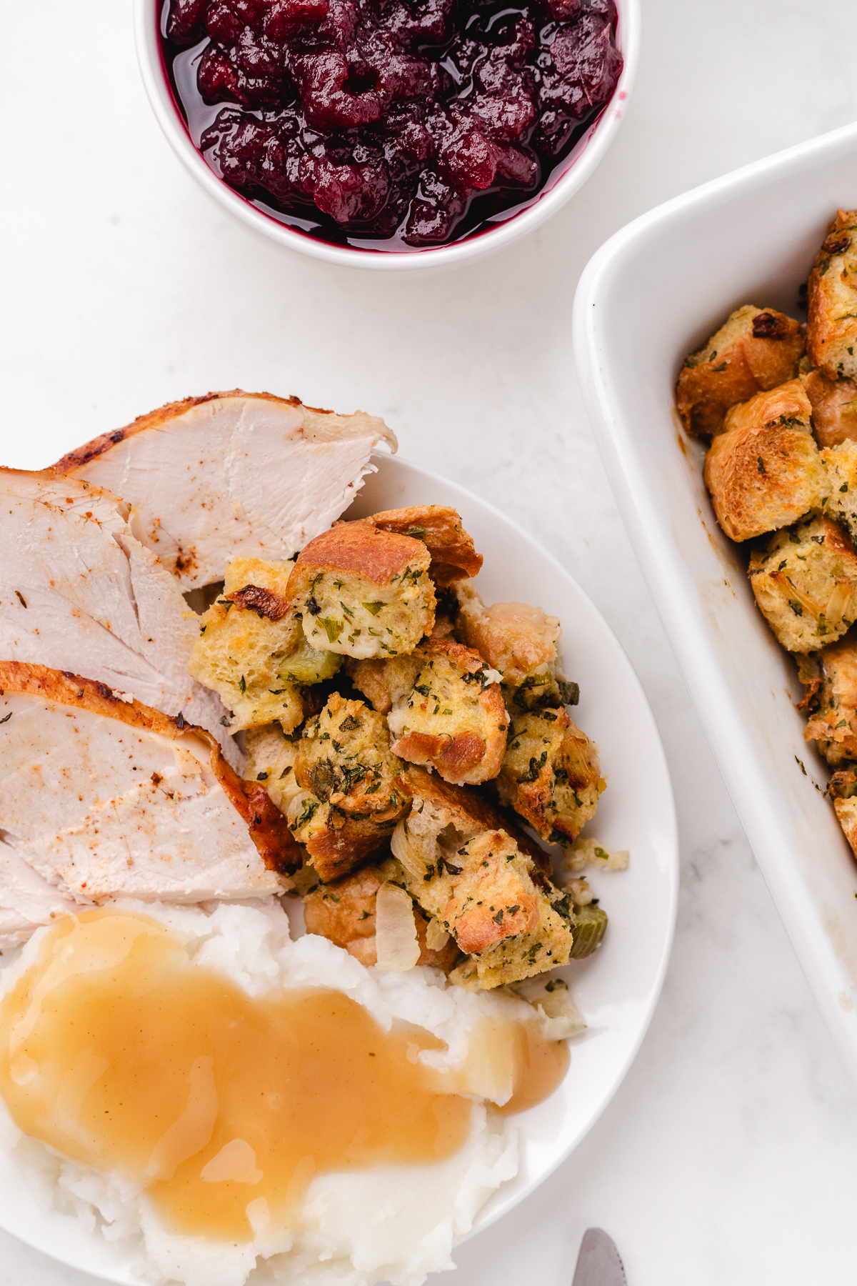 thanksgiving dinner including stuffing turkey mashed potatoes gravy and cranberry sauce on a white table cloth