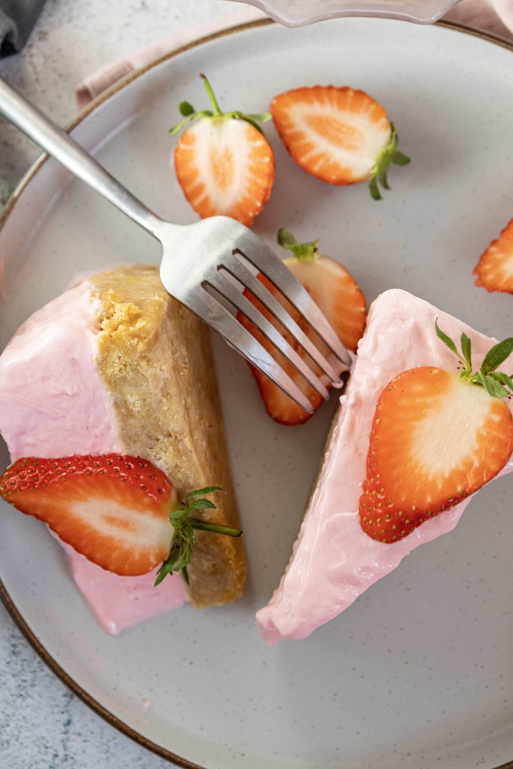 Two slices of strawberry cheesecake on a plate with fresh strawberries