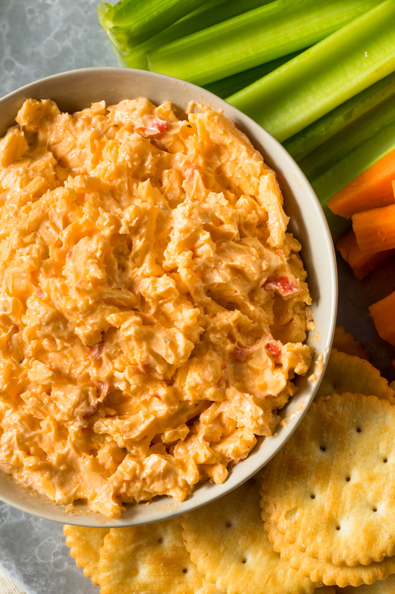 grandmas old fashioned pimento cheese from scratch with mayo and sharp cheddar cheese in a white bowl with crackers and celery