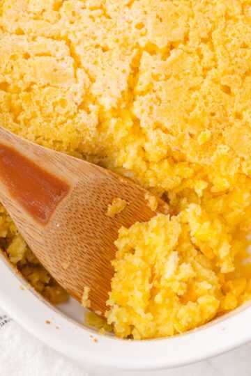 Corn casserole being served with a wooden spoon.