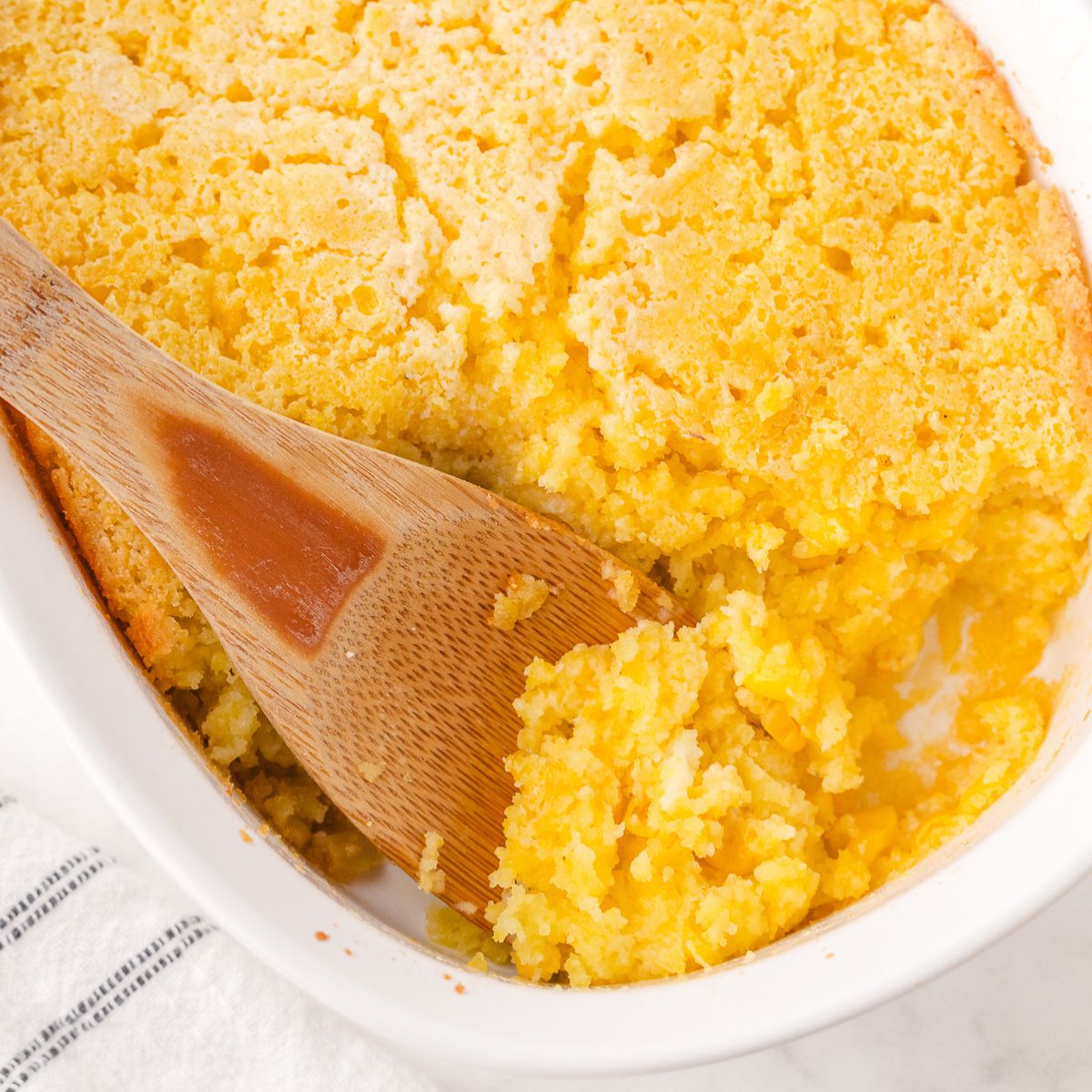 Corn casserole being served with a wooden spoon.