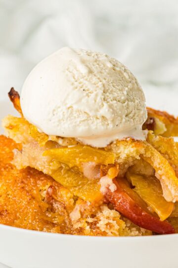 Old fashioned peach cobbler served in a white bowl is vanilla ice cream on top