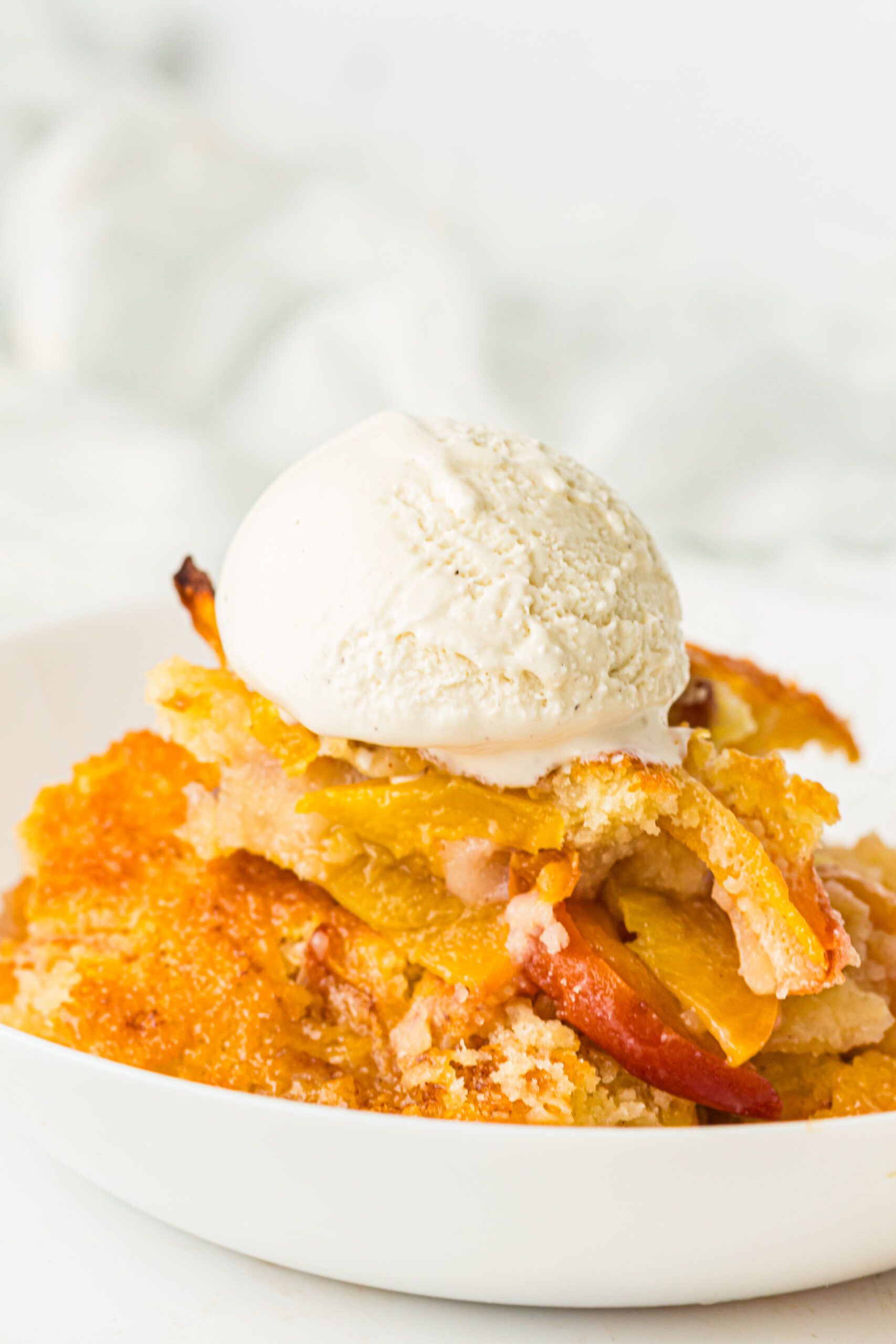 Slice of peach cobbler with ice cream on top.