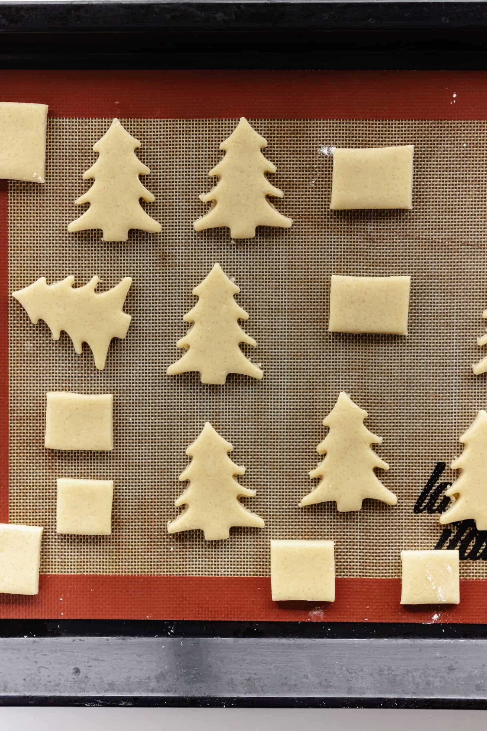 Christmas tree and present shaped butter cookie dough on a baking sheet
