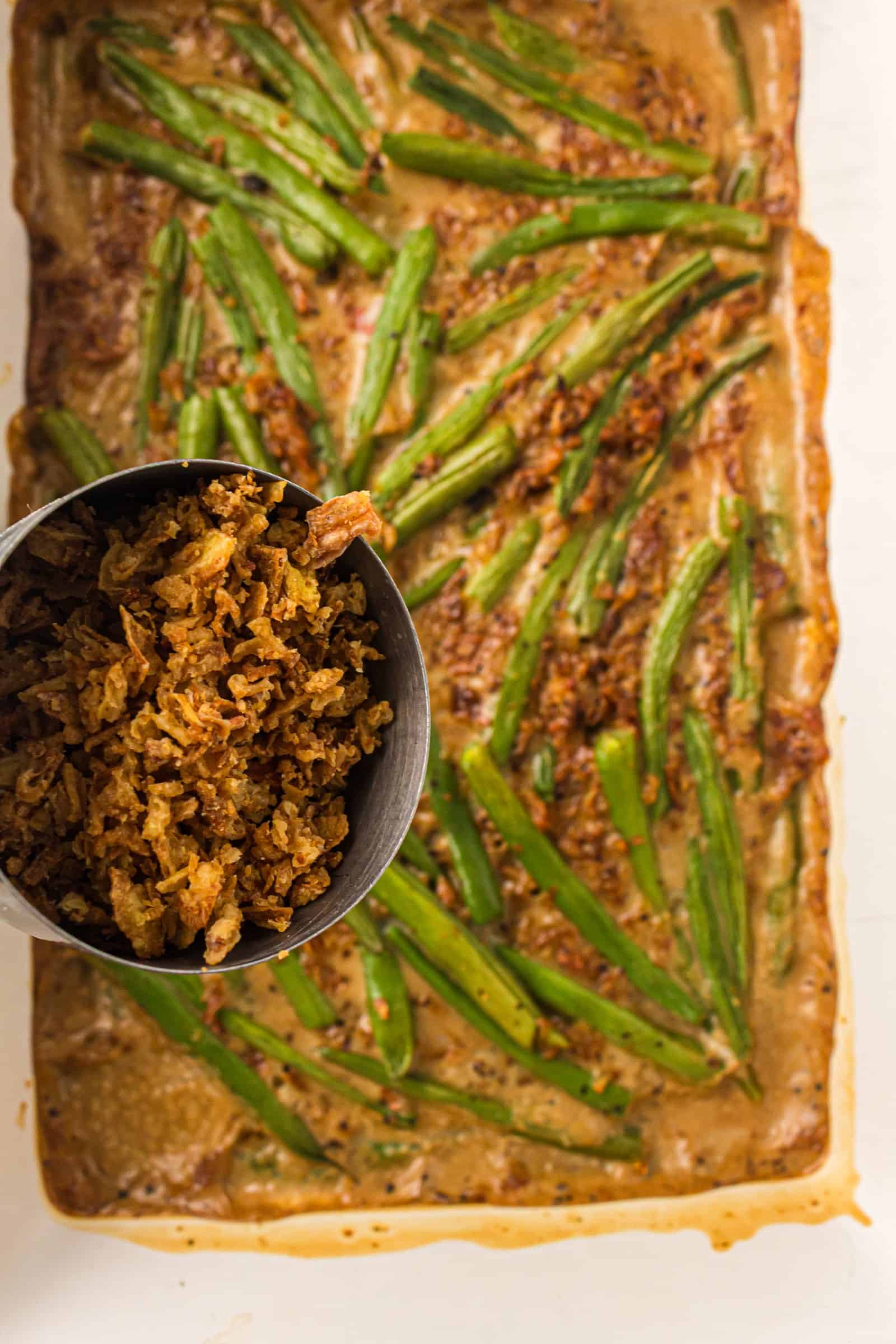 French fried onions being sprinkled over green bean casserole.