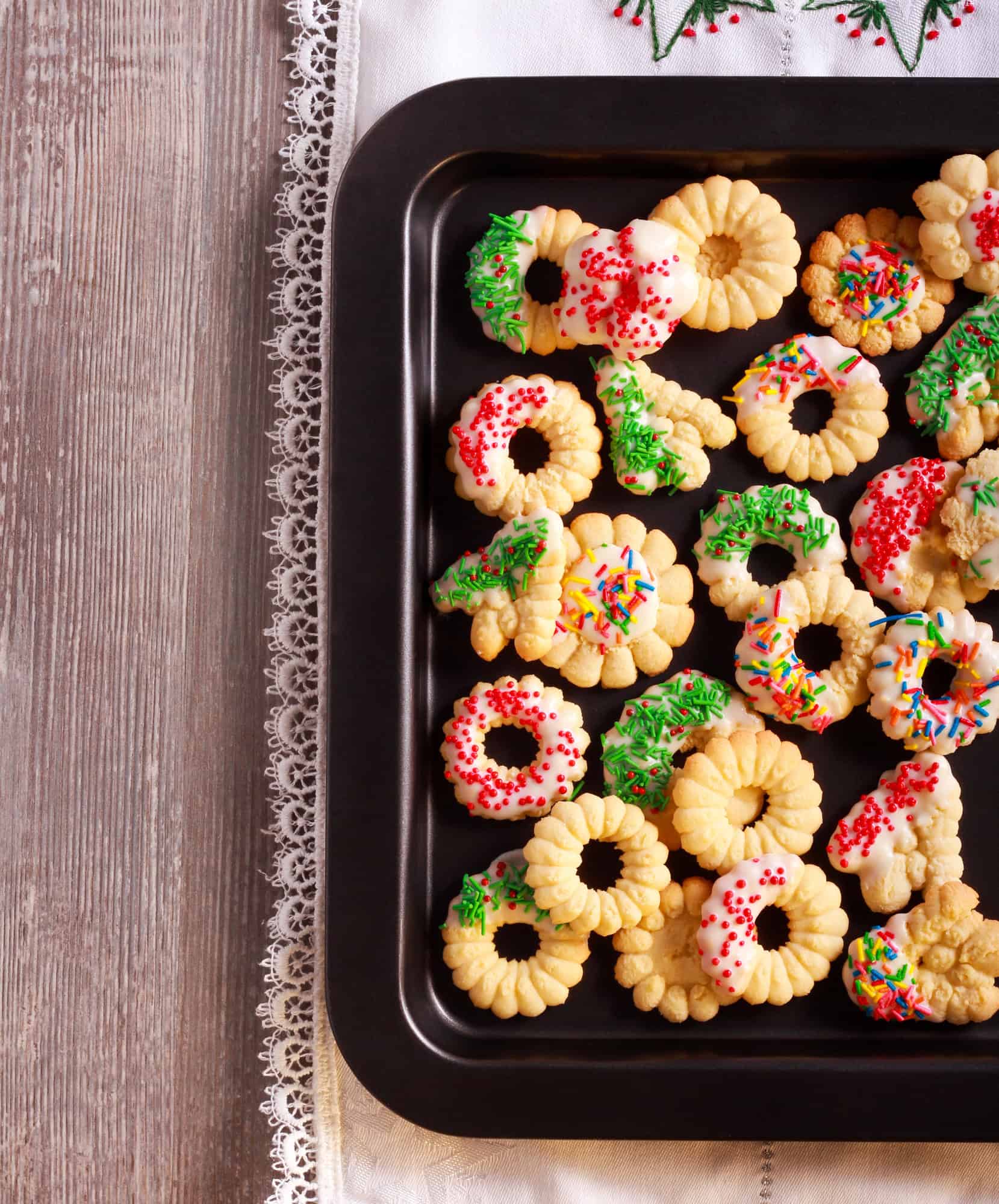 Old fashioned spritz cookies with icing and Christmas sprinkles on a baking tray
