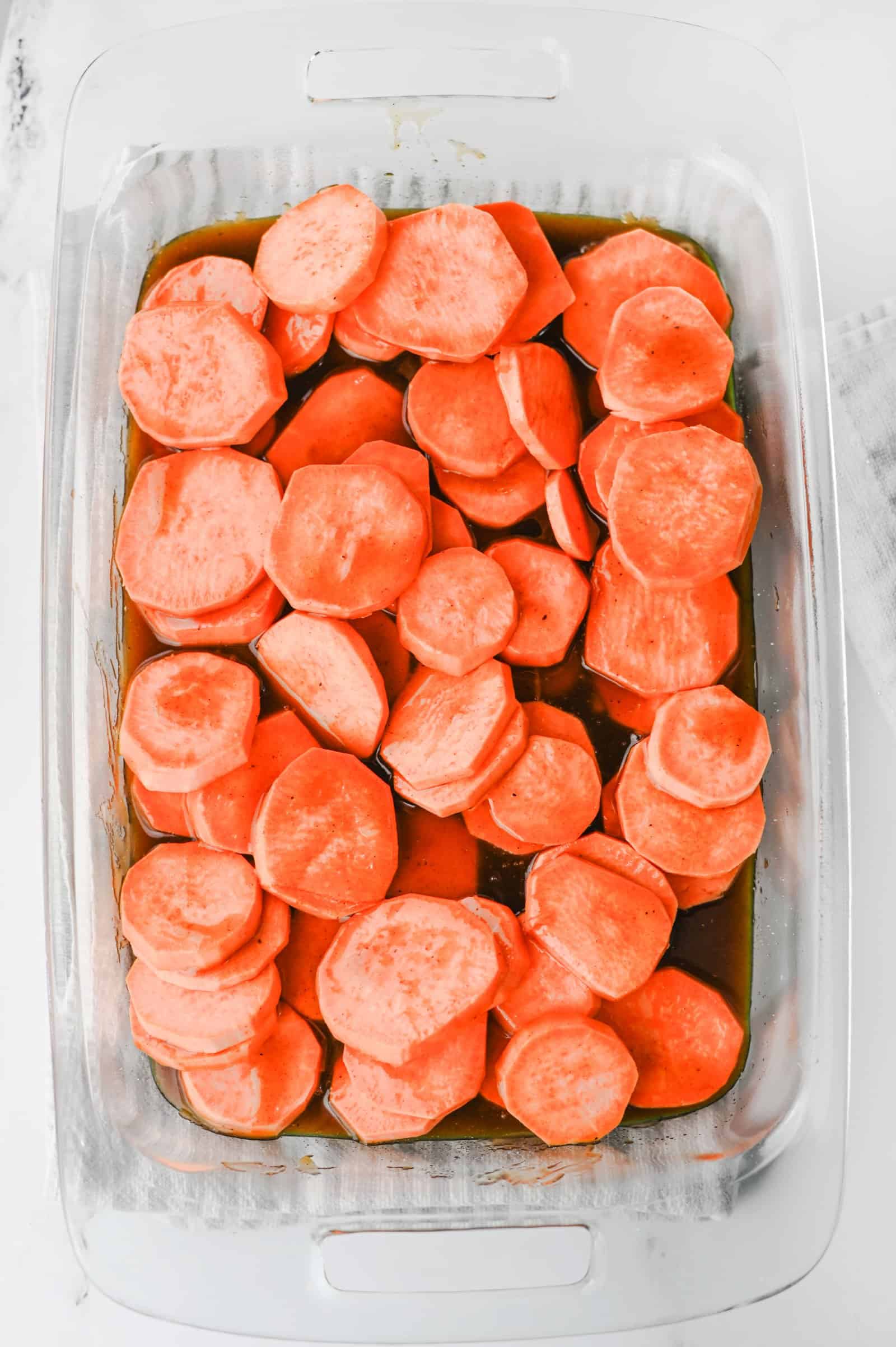 Candied syrup poured over sliced sweet potatoes in a baking dish.