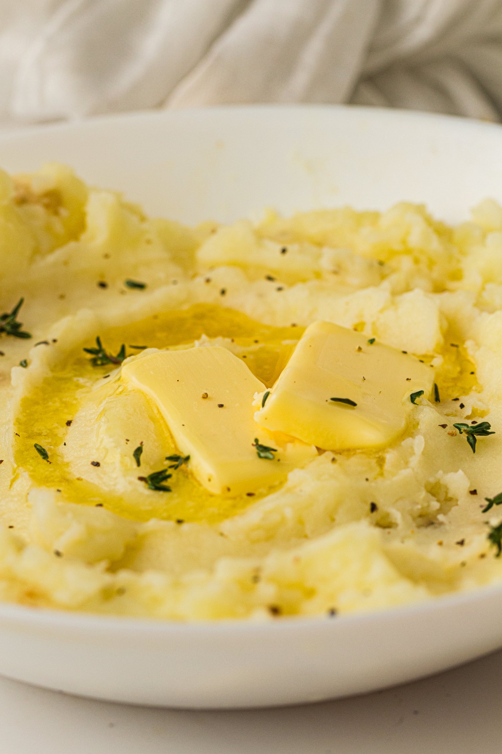 Old fashioned mashed potatoes in a white bowl with melting butter and fresh herbs.