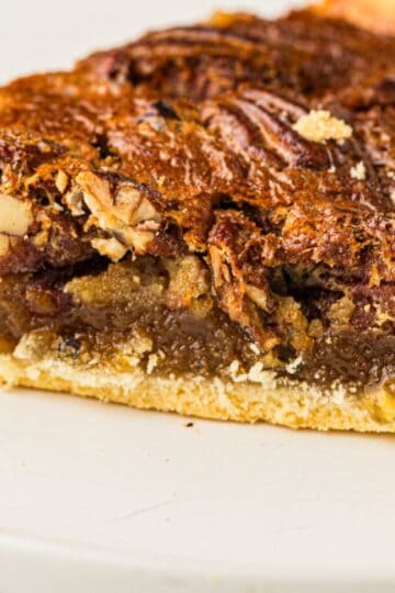 Slice of old fashioned pecan pie with brown sugar on a white plate.