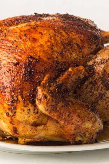 Whole roast turkey with butter under the skin on a white platter.