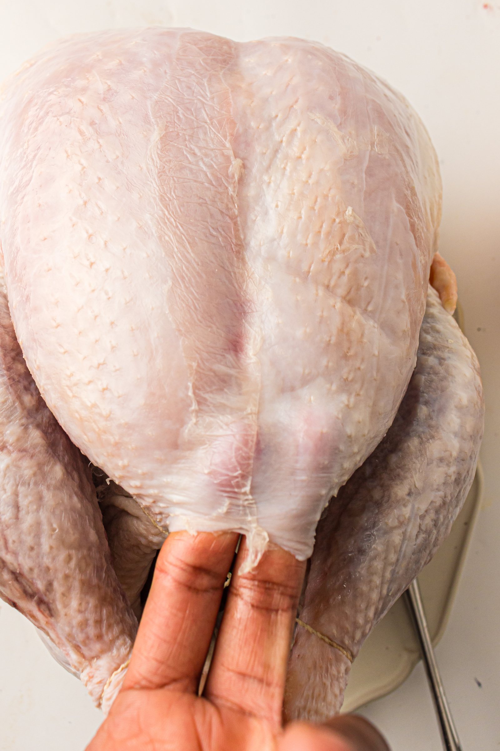 Hand loosening the turkey skin to spread butter underneath.