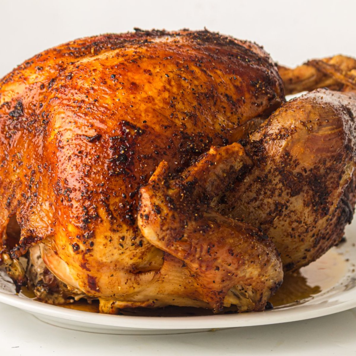 Whole roast turkey with butter under the skin on a white platter.