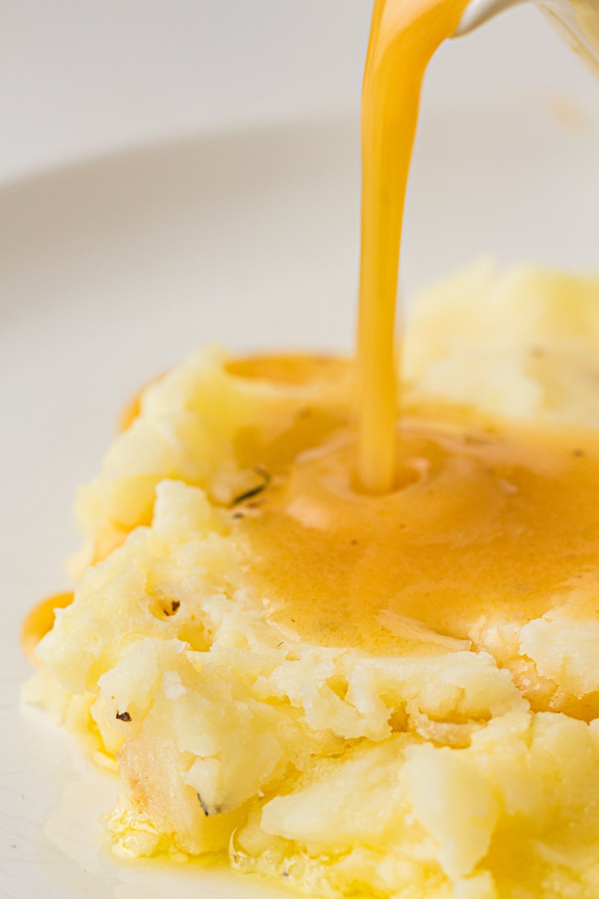 Homemade turkey gravy being poured over mashed potatoes.
