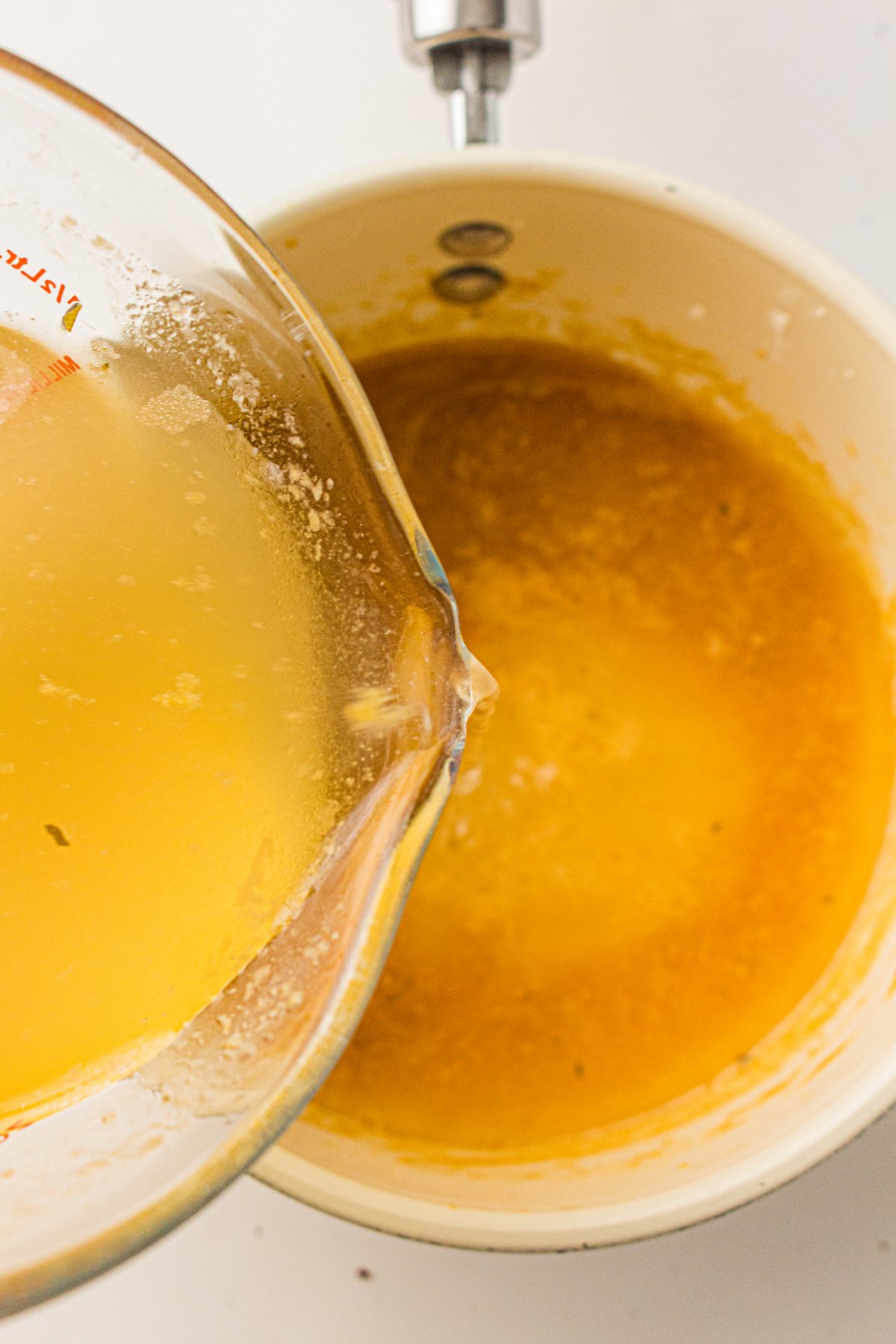 Warm broth being poured into the roux for turkey gravy.